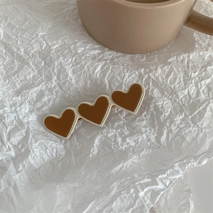 Close-up of triple heart-shaped hair clip with brown finish on white textured paper