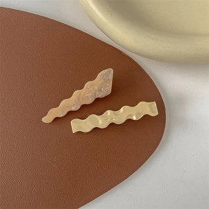 Close-up of wavy marble pattern and cream yellow matte hair clips on leather mat