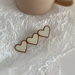 Detail of three-heart shaped hair clip in matte beige and brown on textured paper