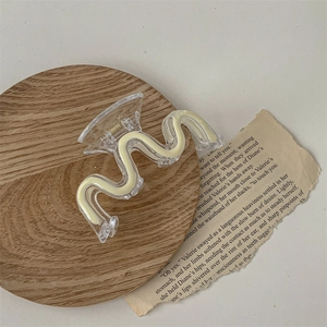 Detailed close-up of a wavy beige acrylic hair claw clip with golden metal spring