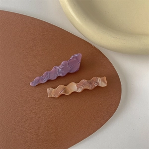 Detail view of two wave-shaped marble texture hair clips on a premium brown leather surface