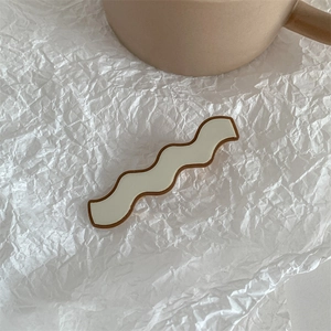 Detail of cream wavy hair clip with brown trim on white textured background
