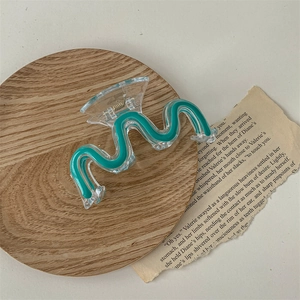 Macro detail of wave hair claw clip in transparent green on rustic wooden tray