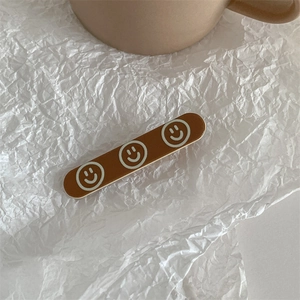 Close-up of brown acrylic duckbill hair clip with white smiley faces on wrinkled paper