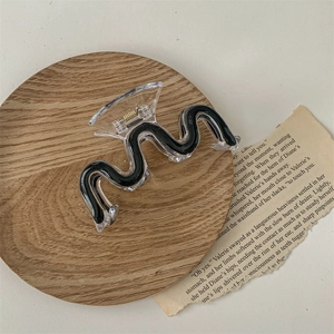Close-up of wavy acrylic hair claw clip in black and clear on minimalist wood tray