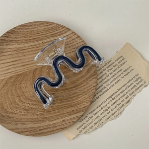 Detail of a wavy acrylic hair claw clip in deep blue, shown on a wooden tray with a retro style