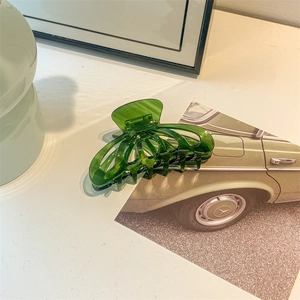 Close-up of a large dark green acetic hair claw clip on a retro background