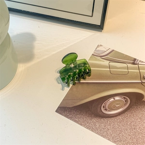 Detailed close-up of dark green acetate hair claw clip on a minimalist desk with card decor