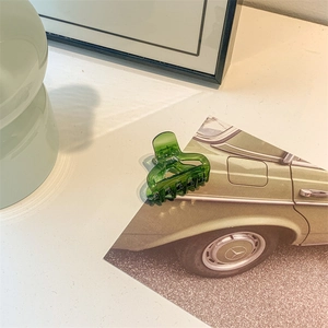 Close-up of translucent emerald green hair claw clip on a vintage decorative card