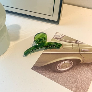 Detail of dark green acetate hair claw with marble texture on a minimalist desk