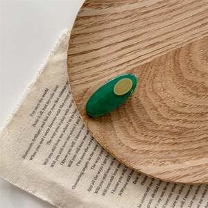 Green marble acrylic hair clip with gold logo detail on vintage wooden tray decor