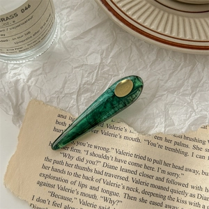 Détail d'une pince à cheveux en acétate vert marbré avec logo doré sur papier vintage