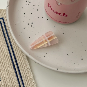 Détail d'une pince à cheveux rose à carreaux sur un plateau en céramique pour un look doux