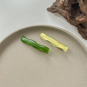 Detail view of wavy resin hair clips in green and yellow on a minimalist display