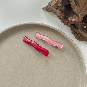 Detail of wavy resin hair clips in dark red and pearlescent pink finishes