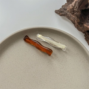 Detail of wavy hair clips in amber brown and transparent glitter resin on ceramic plate