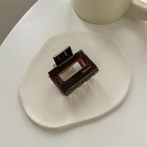 Detail view of a chocolate brown rectangular acrylic hair claw clip on a tray