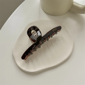 Detail of a glossy chocolate brown hair claw clip on a white ceramic plate with gold text