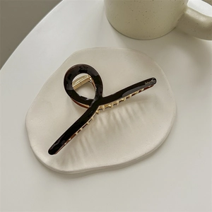 Detailed close-up of dark brown tortoiseshell hair claw clip with golden metal teeth