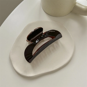 Detail view of a glossy dark brown tortoiseshell claw clip on a white ceramic tray