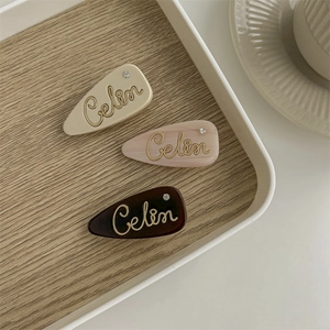Three-piece French acetate hair clips set with rhinestones and cursive lettering on wood