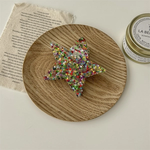 Détail de la pince à cheveux en étoile avec paillettes colorées sur plateau en bois