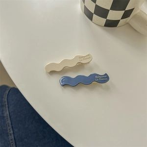 Close-up of wavy cream and navy blue resin hair clips with elegant brand lettering