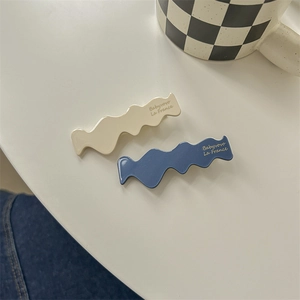 Detailed close-up of blue and white wavy hair clips with elegant gold lettering on surface