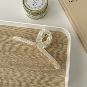 Detail of cream marble acetate hair claw clip with golden spring on a white tray