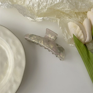 Detail view of large acetate hair claw clip with pearlescent finish on artistic background