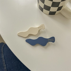 Close-up of wavy blue and beige hair clips with glossy resin finish on white surface