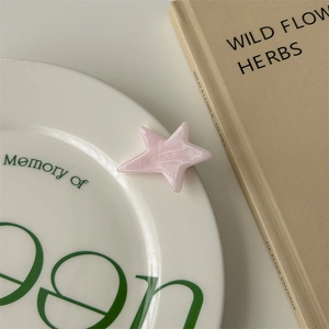 Macro detail of a pink acetate star hair clip with pearlescent finish on a ceramic plate