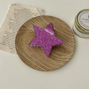 Gros plan d'une pince à cheveux étoile à paillettes violettes sur plateau en bois