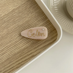 Detail view of pink resin hair clip with gold cursive text and a sparkling rhinestone