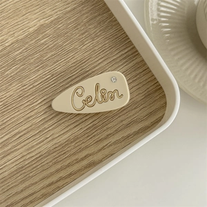 Detailed view of a cream-colored teardrop hair clip with Celin script and rhinestone