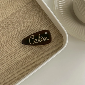 Detailed shot of a dark brown acetate hair clip featuring gold Celin lettering and rhinestone