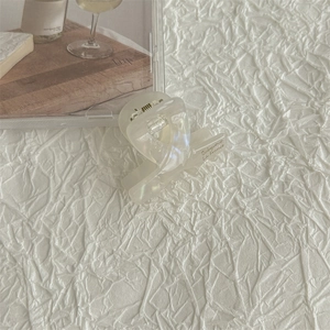Detail of a pearlescent cream mini hair claw clip on soft white textured fabric