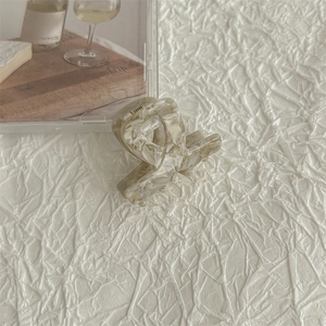 Close-up of a mini acetate hair claw clip with cream marble pattern on textured paper