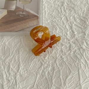 Detailed view of an amber acetate hair claw clip with cross design on white textured fabric