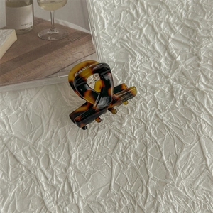 Detail of tortoise shell acetate hair claw with engraved branding on a paper background