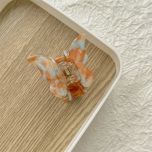 Vue détaillée d'une pince à cheveux papillon en acétate orange sur un plateau en bois
