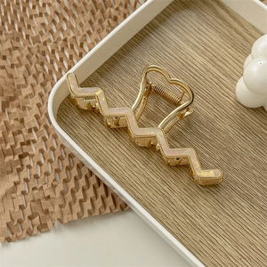 Macro detail of wave-shaped golden hair claw clip with pearl white resin inlay textures