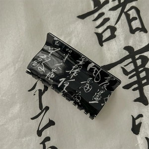 Close-up of minimalist black hair claw with white Chinese calligraphy art patterns