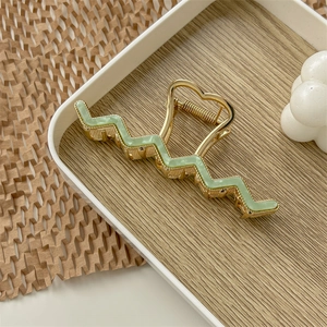 Detailed view of elegant gold metal wave hair claw clip with green enamel and heart design