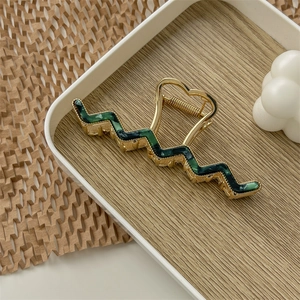 Close-up of golden wave hair claw clip with dark green marble texture and metal spring