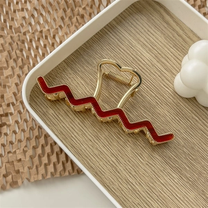 Macro shot of gold metal hair claw with burgundy wave pattern on wooden tray