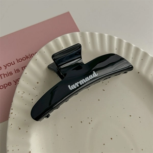 Dettaglio di pinza per capelli nera in resina con scritte bianche in un piatto di ceramica