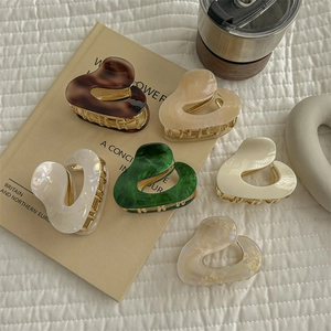 Irregular heart-shaped acetate hair claw clips in six colors on minimalist background