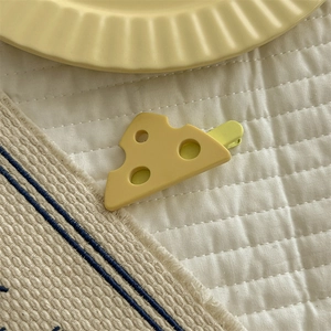Detailed macro view of a playful yellow cheese-shaped hair claw clip on soft fabric