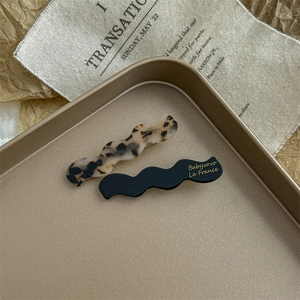 Detail of tortoise shell and black acetate hair clips with gold logo on metal tray